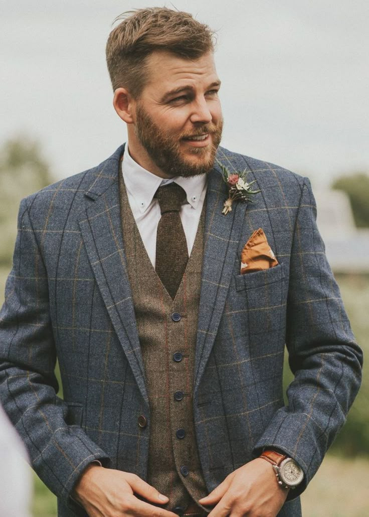 a man with a beard wearing a suit and flower in his lapel is looking at the camera