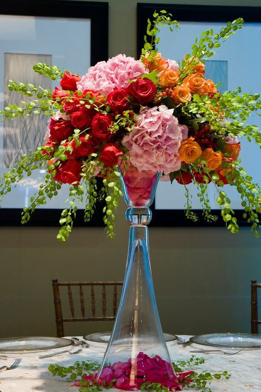 a vase filled with pink and red flowers on top of a white table covered in greenery