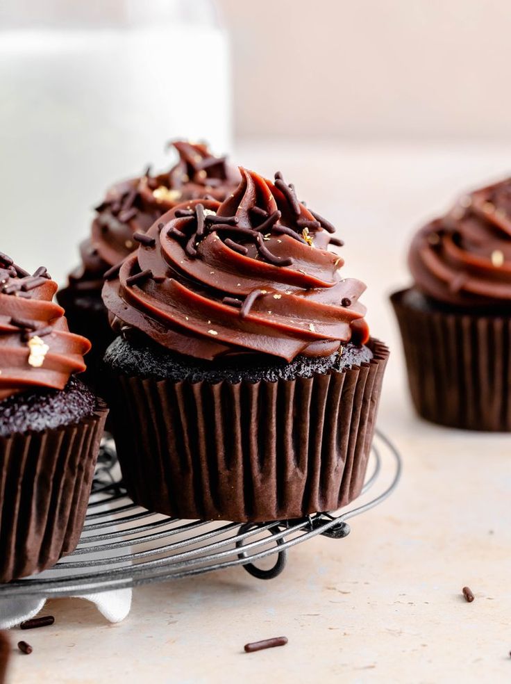 three chocolate cupcakes on a wire rack next to a glass of milk