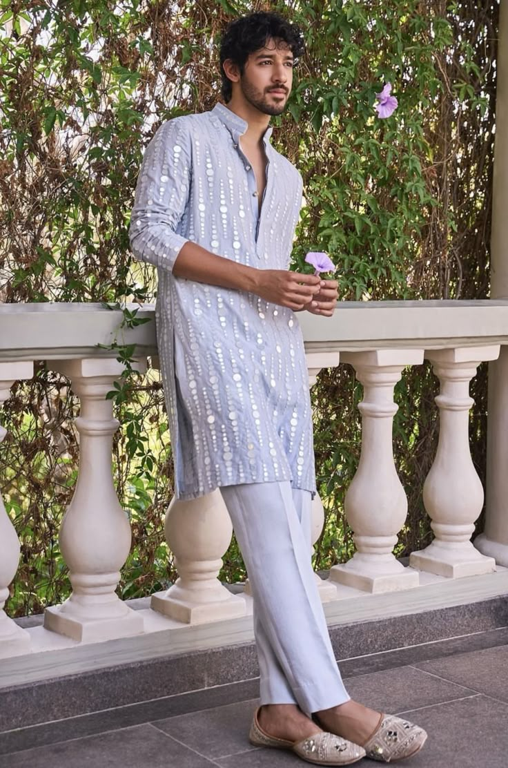 a man is standing on the porch with his hand in his pocket and holding a flower