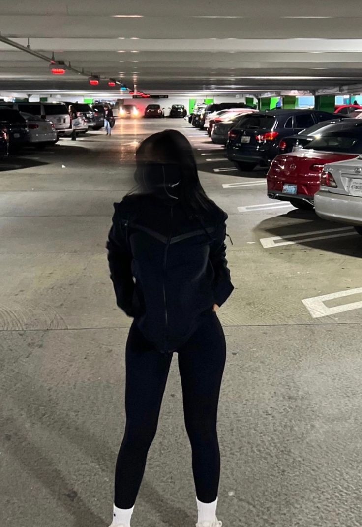 a woman standing in the middle of a parking garage with her back turned to the camera