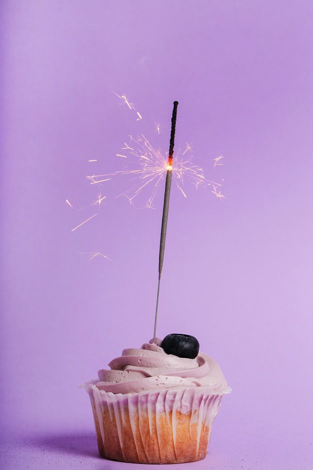 a cupcake with a sparkler sticking out of it's side on a purple background