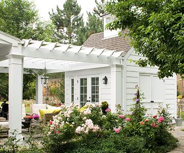 an outdoor living area with white furniture and flowers in the foreground, surrounded by greenery