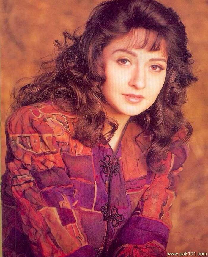 a woman with long dark hair wearing a purple shirt and posing for a photo in front of a brown background