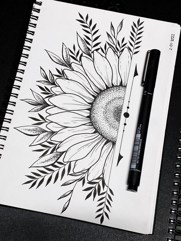 a sunflower drawing on a notebook with a black pen and some leaves around it