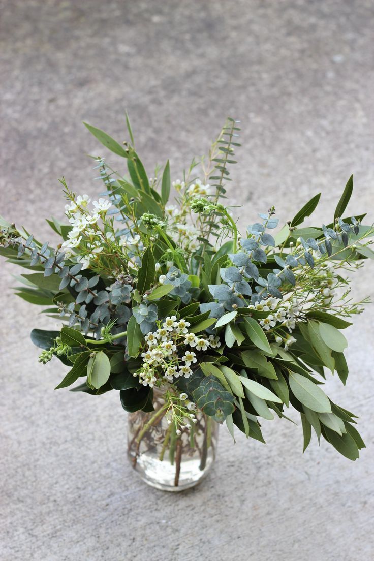 a glass vase filled with lots of green leaves and white flowers on top of cement