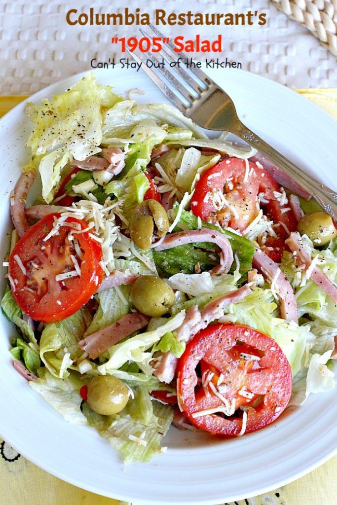 a salad with tomatoes, lettuce, olives and cheese is on a white plate