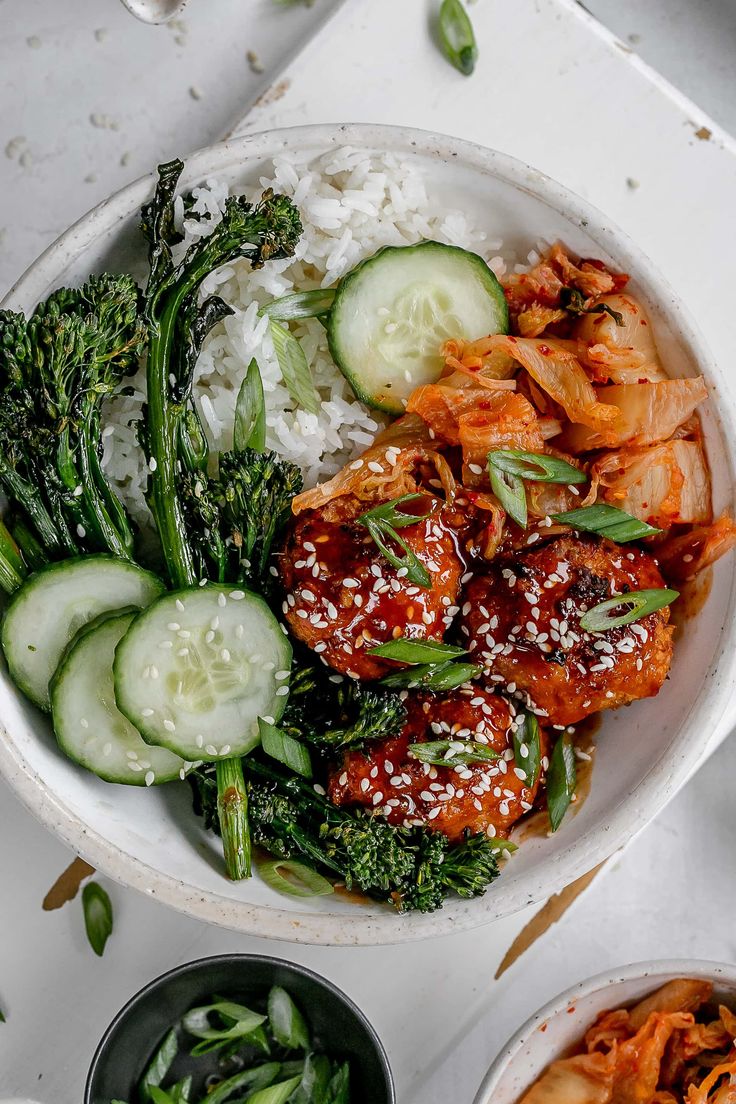 a white bowl filled with meat and veggies next to bowls of rice, broccoli and cucumbers