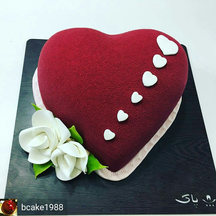 a red heart shaped cake with white hearts on it's side and flowers in the middle