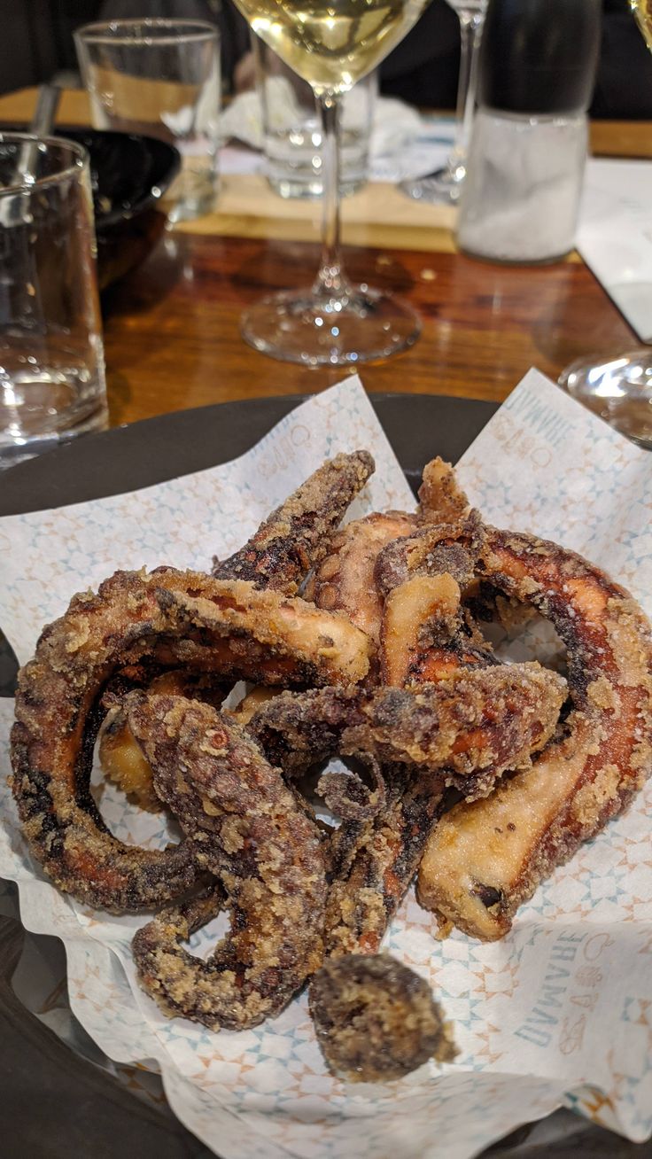 fried octopus rings are on a plate with wine glasses in the backgroung