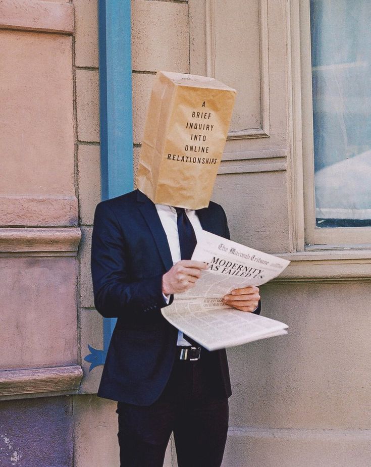 a man with a paper bag on his head is reading the newspaper while standing in front of a building