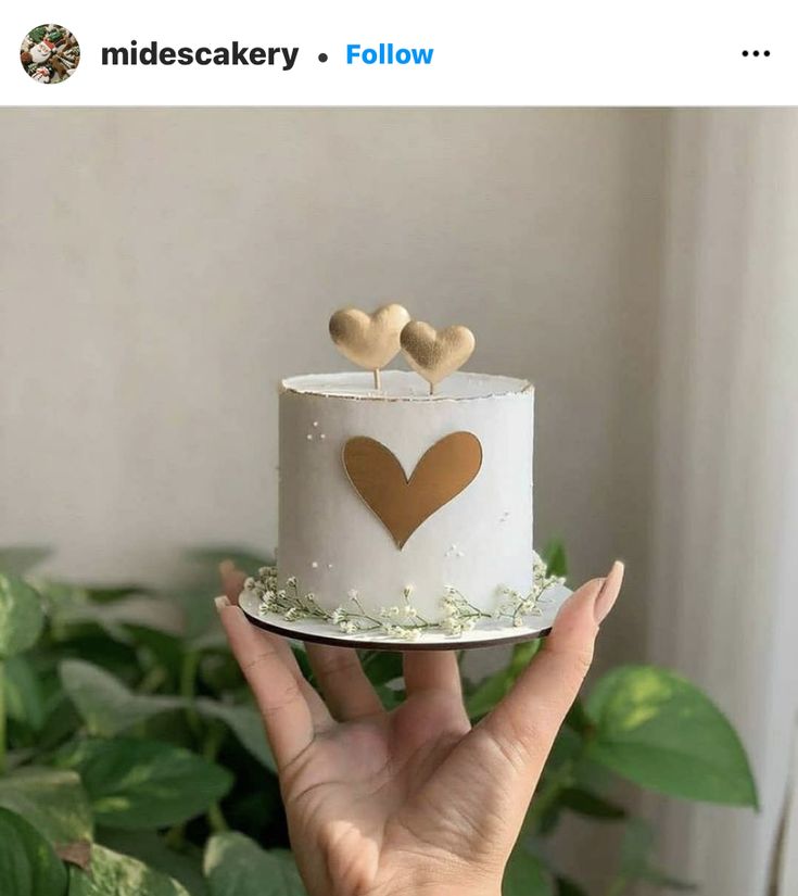 a hand holding a white cake with gold hearts on top and two brown hearts on top