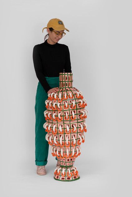 a woman standing in front of a large vase made out of orange and white cups