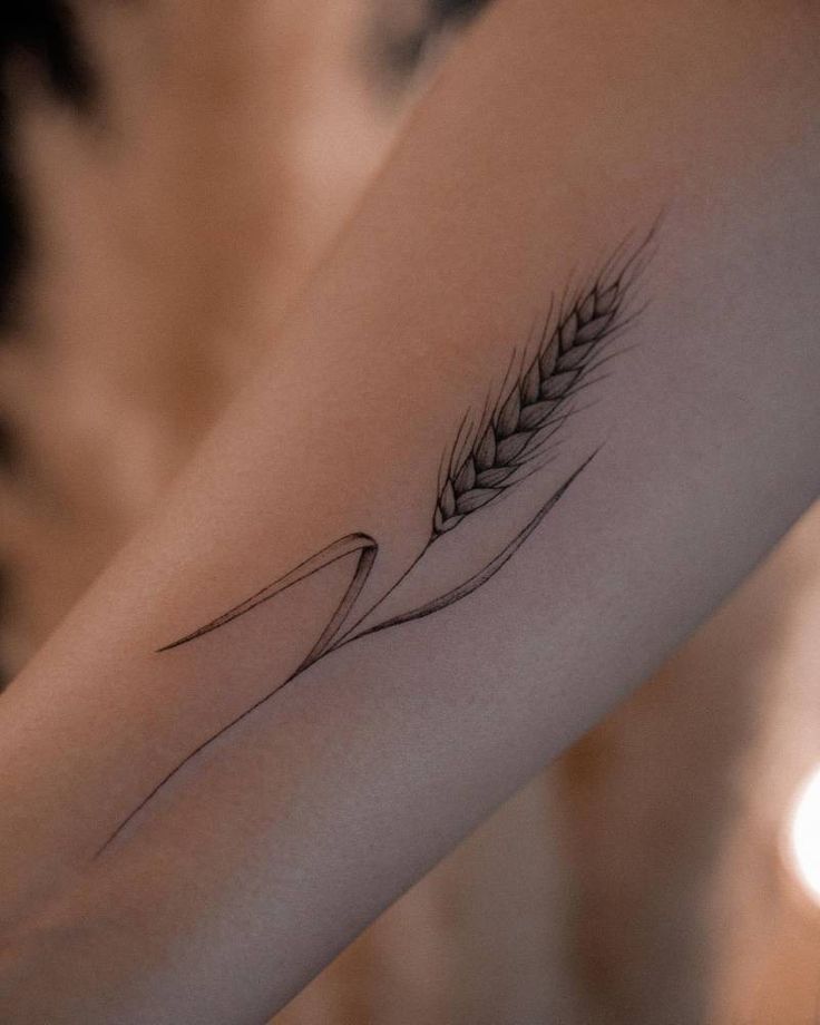 a woman's arm with a tattoo on it that has a wheat stalk in the middle