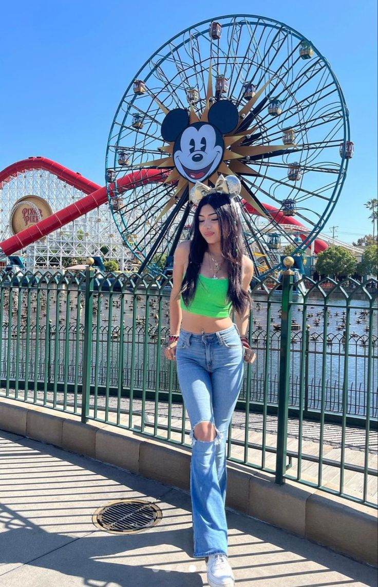 a woman standing in front of a ferris wheel with mickey mouse head on her head