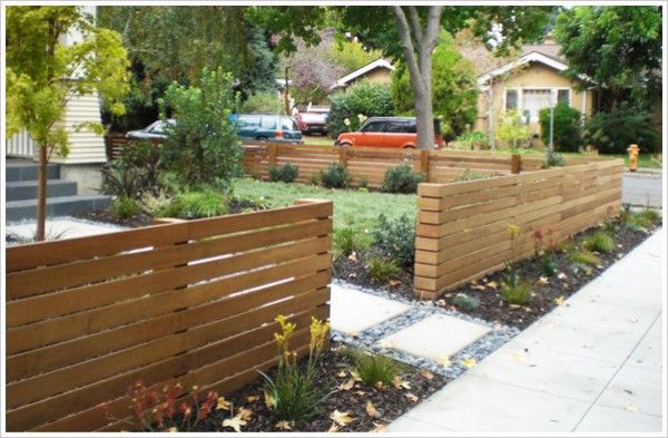 a wooden fence in the middle of a yard with cars parked on the street behind it