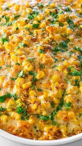 a white casserole dish filled with corn and cheese, garnished with parsley