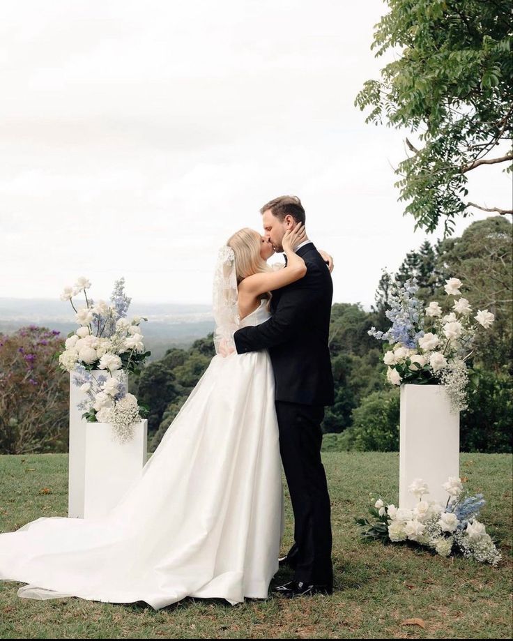 a bride and groom kissing in front of their wedding arch with flowers on the side