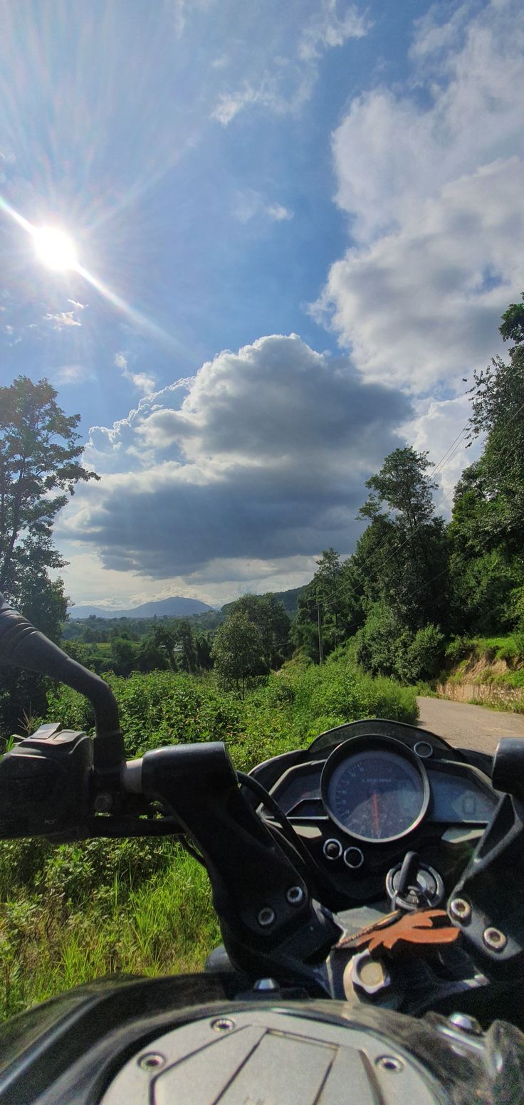 a motorcycle is parked on the side of the road near some grass and trees, while the sun shines brightly in the distance