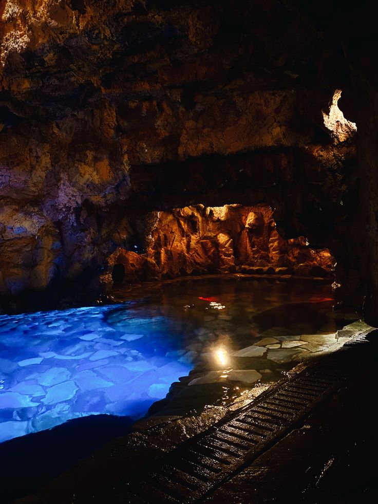 an underground swimming pool with blue lights in the water and rocks on either side at night