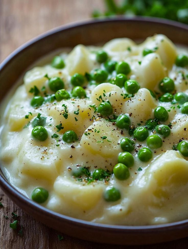 a bowl filled with pasta and peas on top of a wooden table