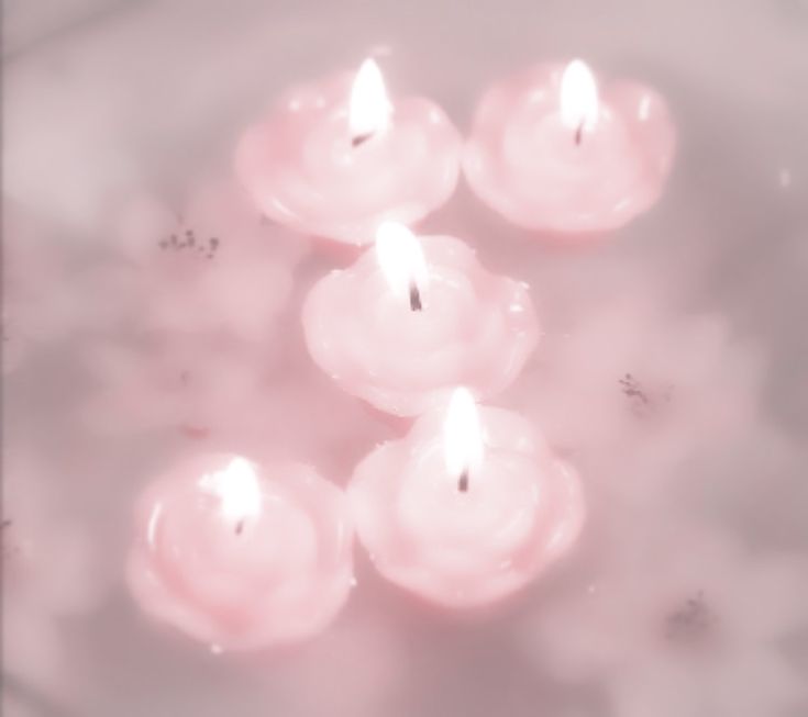 several lit candles floating in water on top of a white tablecloth with pink hues