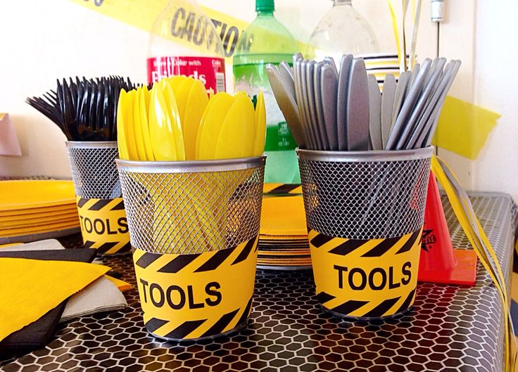 there are two cups that have tools in them on the table with yellow and black tape