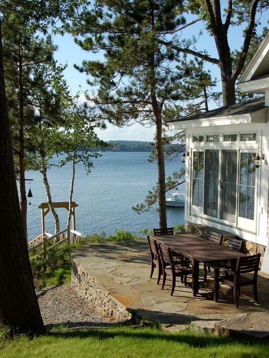 a table and chairs are outside by the water's edge with trees around it