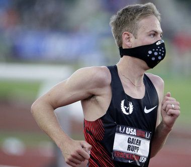 a man wearing a face mask while running in a race track with his hands on his hips