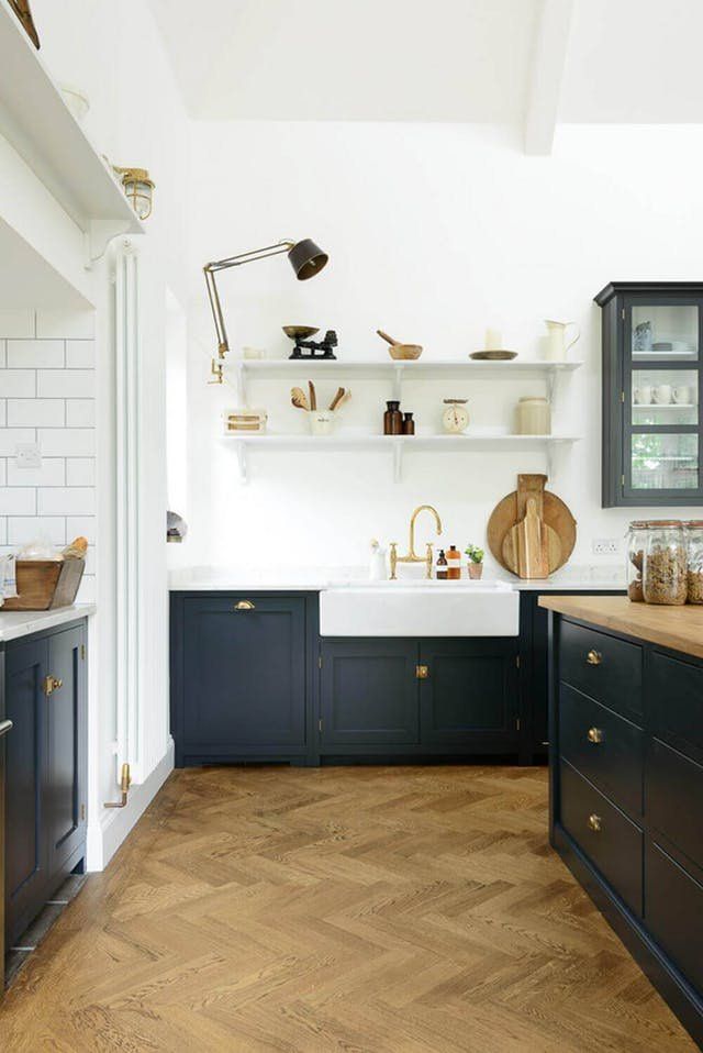 a kitchen with wooden floors and black cabinets, white walls and open shelving above the sink