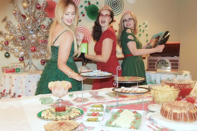 three women in green dresses standing around a table with desserts and candies on it