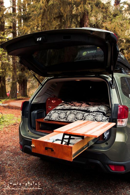 an open hatchback car trunk with a bed on it's back in the woods