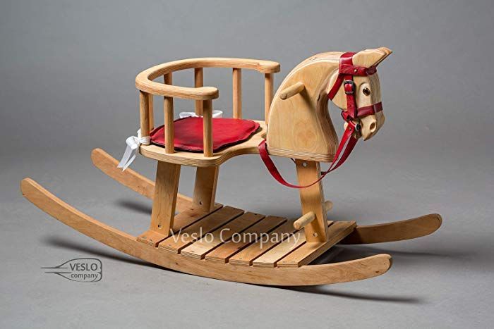 a wooden rocking horse with red seat and harness on it's back, in front of a gray background