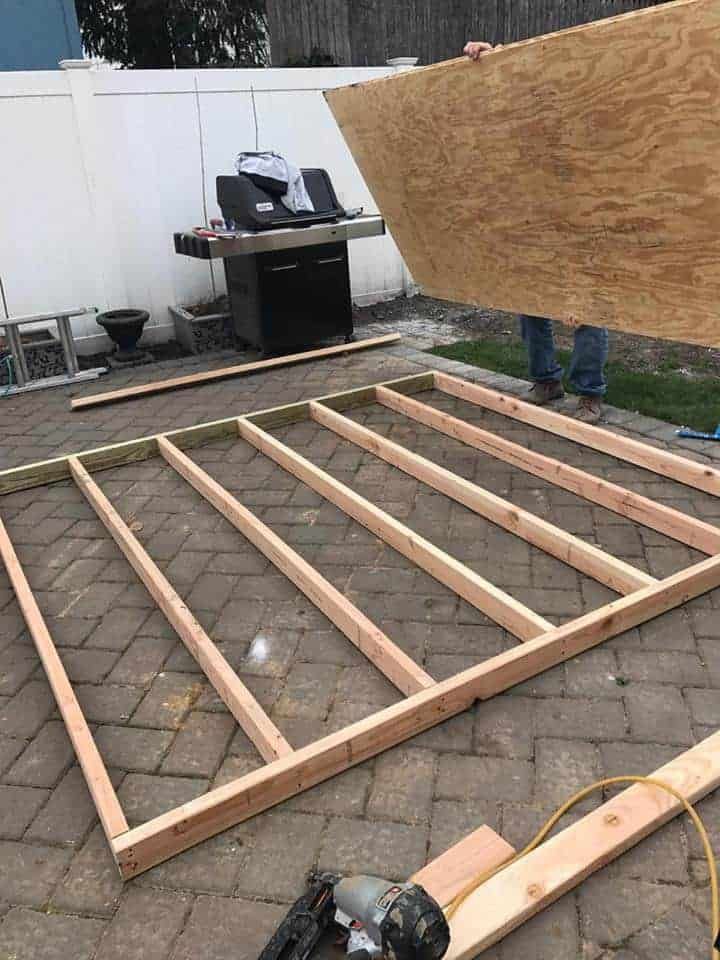 a man standing on top of a wooden floor in the middle of a yard next to a bbq