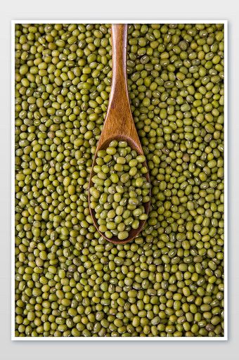 a wooden spoon filled with green peas on top of a white table next to a wall