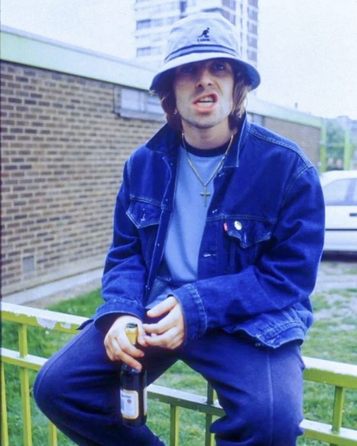 a man sitting on a rail with a bottle in his hand and wearing a hat