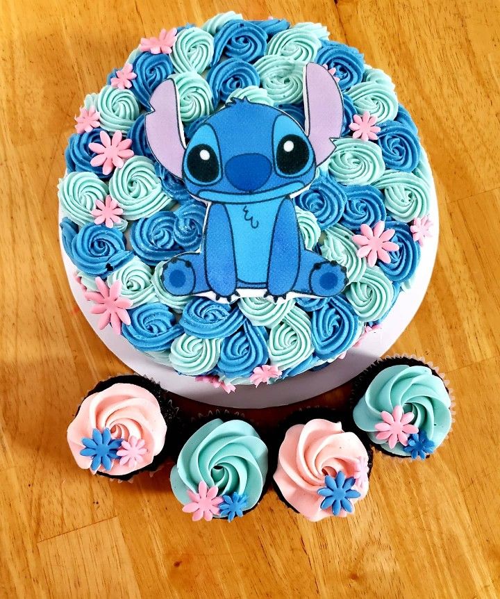 a blue and pink cake sitting on top of a wooden table next to cupcakes