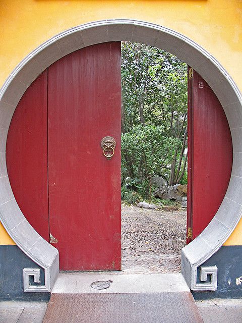 an open red door leading into a lush green area with rocks and trees in the background