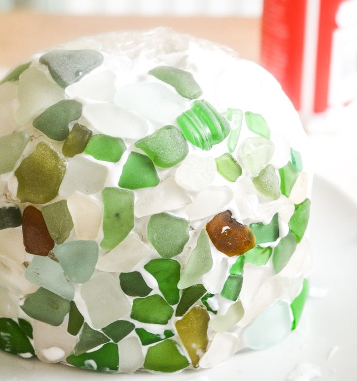 a white plate topped with a green and white cake covered in sea glass shards next to a can of soda