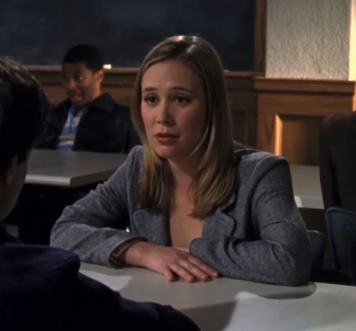 a woman sitting at a table in front of a man who is talking to her