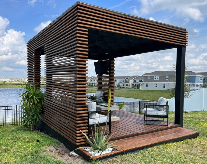 a wooden gazebo sitting on top of a lush green field next to a lake