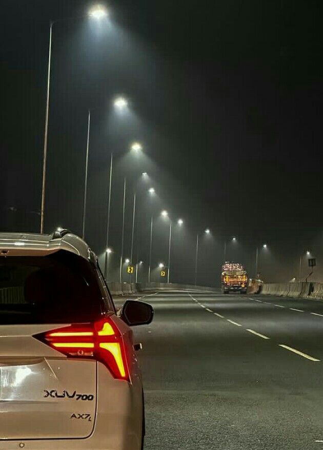 the back end of a car on a road at night with street lights in the background