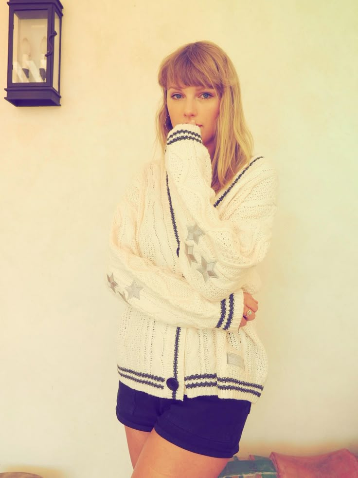 a woman standing in front of a wall with her hands on her face and wearing shorts