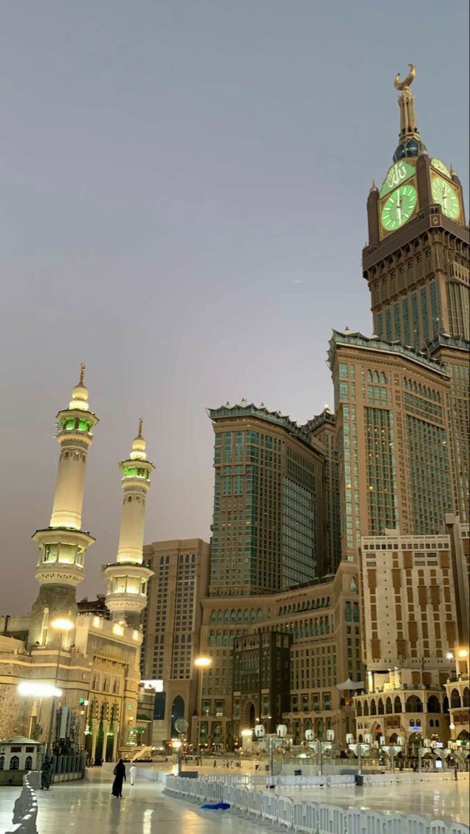 a clock tower in the middle of a large city at night with tall buildings behind it