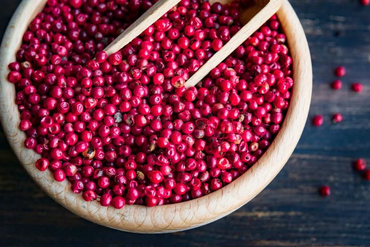 a wooden bowl filled with cranberry seeds and two spoons on top of it