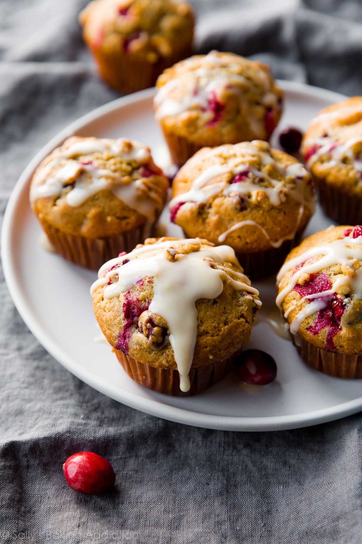 a white plate topped with muffins covered in icing and cranberries