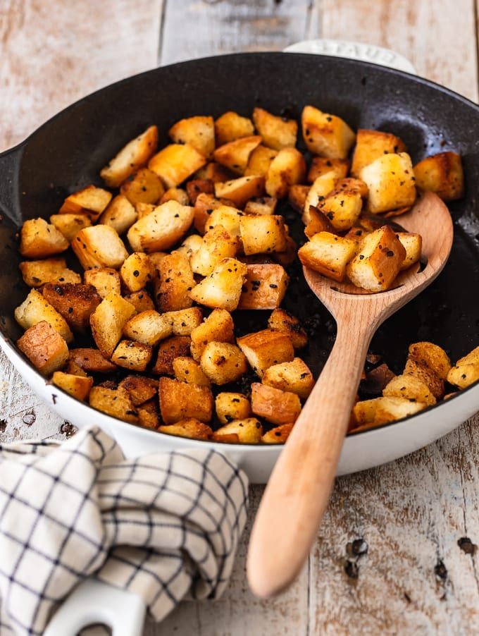 a skillet filled with cooked potatoes on top of a wooden table next to a tea towel