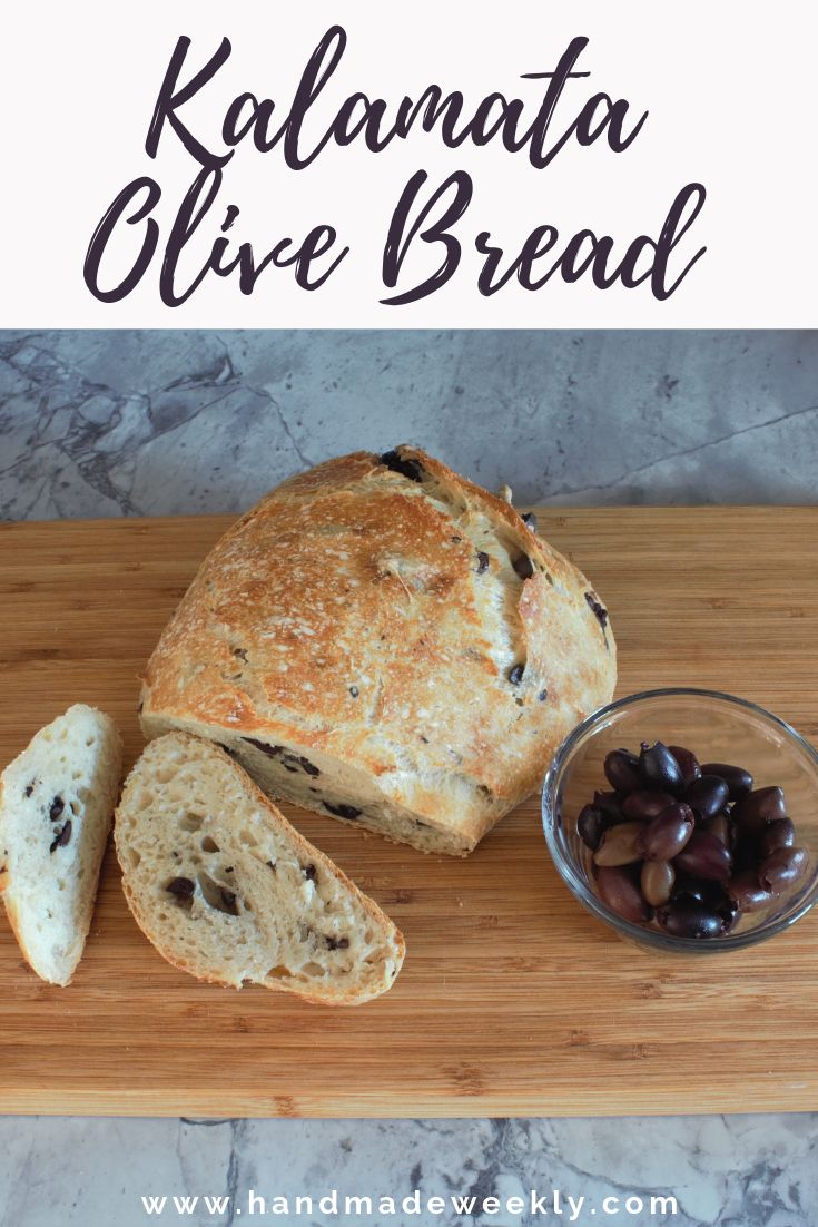 a loaf of bread sitting on top of a wooden cutting board next to olives