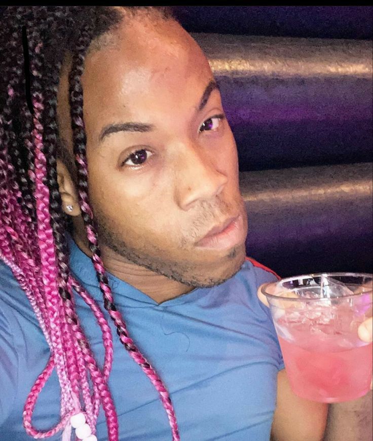 a man with pink dreadlocks holding a drink and looking at the camera while wearing a blue shirt