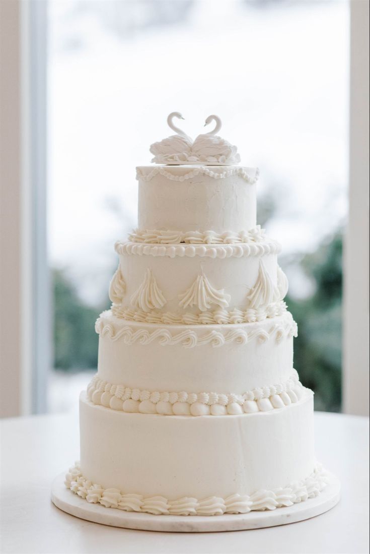 a three tiered wedding cake sitting on top of a white table next to a window